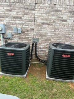 Two air conditioners are sitting next to each other in front of a brick wall.