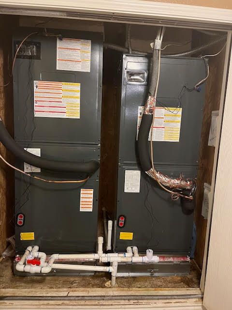 Two air conditioners are stacked on top of each other in a closet.