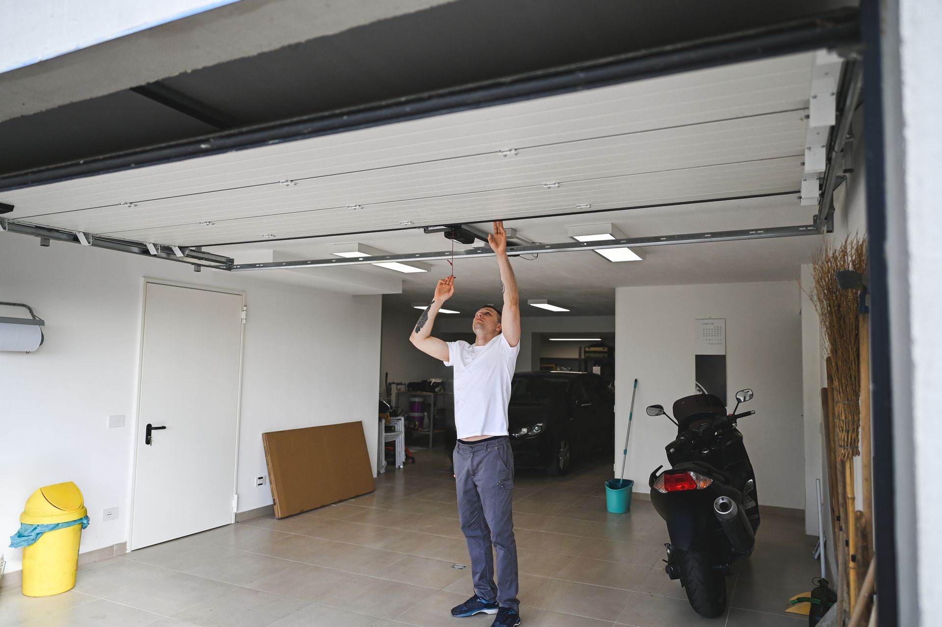 A man extends his arm toward the ceiling, performing garage door repair in the garage.