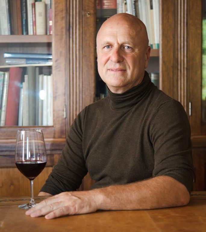 Quattro bottiglie di vino su uno scaffale, con tappi neri, verdi e rossi ed etichette bianche.