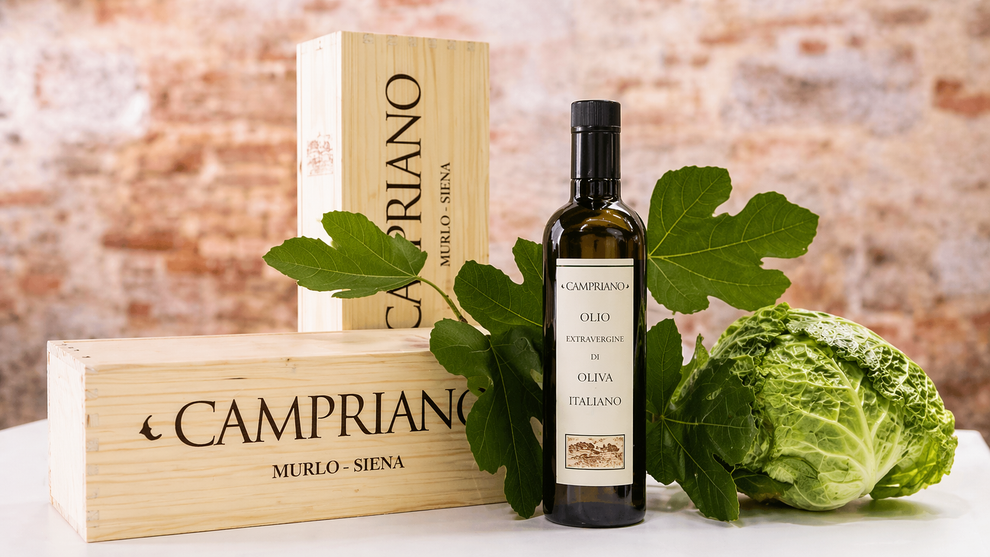 Bottiglia di olio d'oliva Campriano con scatole di legno e foglie di lattuga verde su uno sfondo rustico.