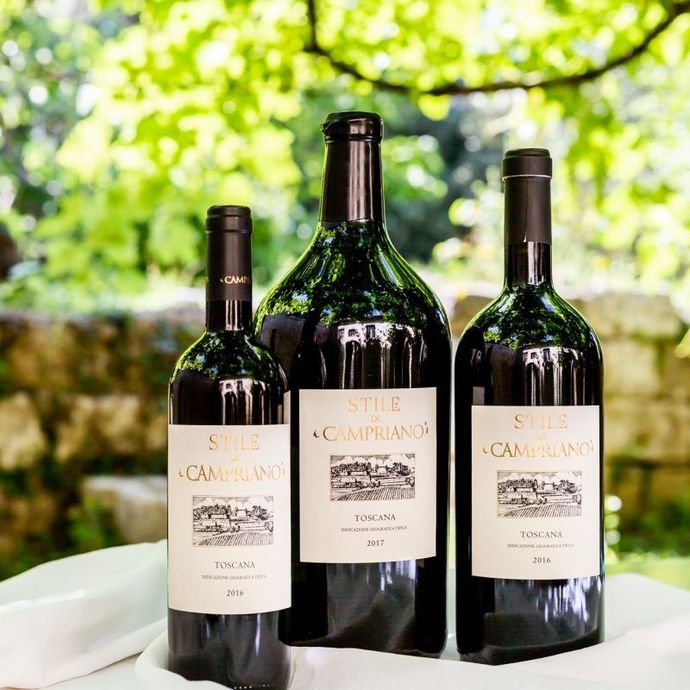 Tre bottiglie di vino su un tavolo all'aperto con uno sfondo sfocato di vigneti verdi.