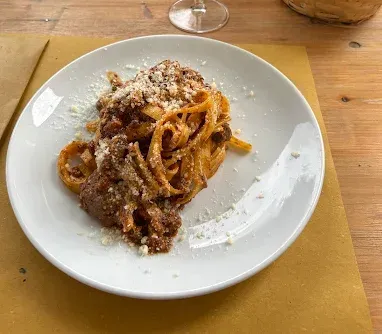 Piatto di spaghetti al ragù e formaggio grattugiato su un tavolo di legno.