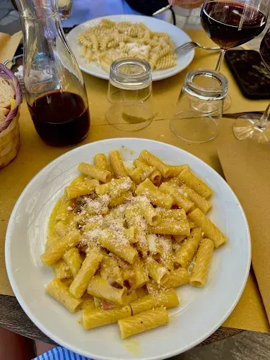 Due piatti di rigatoni con formaggio grattugiato su un tavolo da ristorante con bicchieri da vino e caraffa.