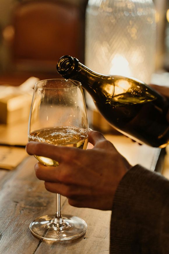 Versare a mano del vino spumante in un bicchiere su un tavolo illuminato da candele.