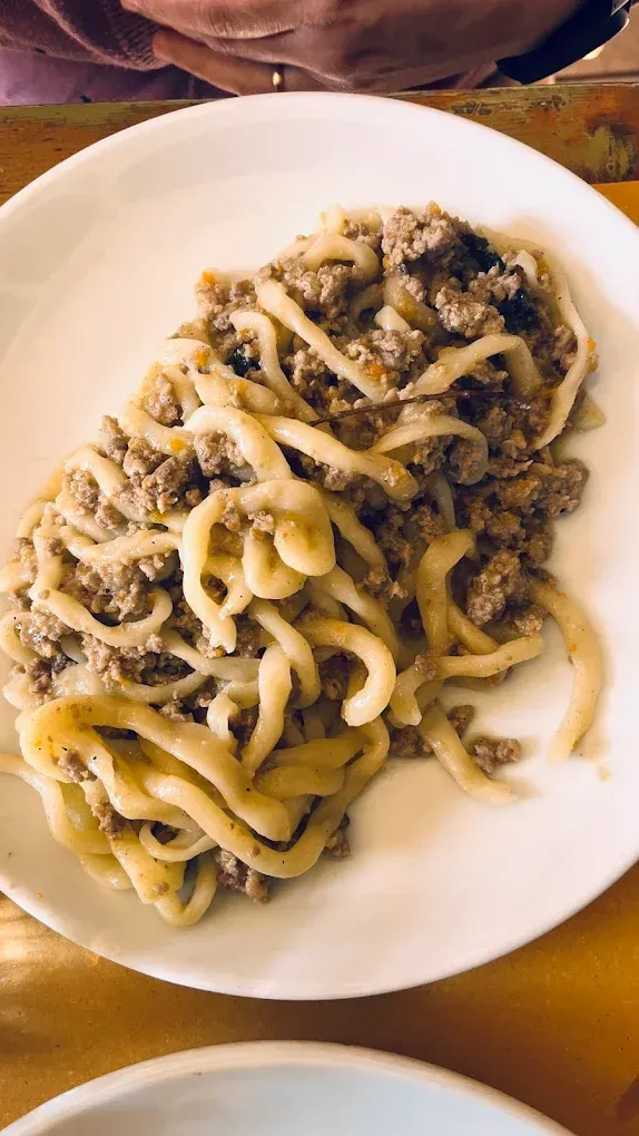 Piatto di pasta al ragù con formaggio grattugiato su un piatto bianco.