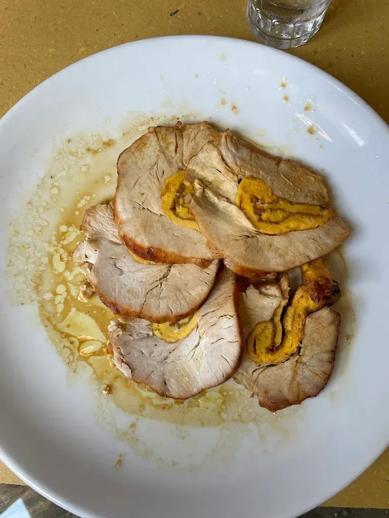 Carne arrosto affettata su un piatto bianco con salsa gialla e un filo d'olio.