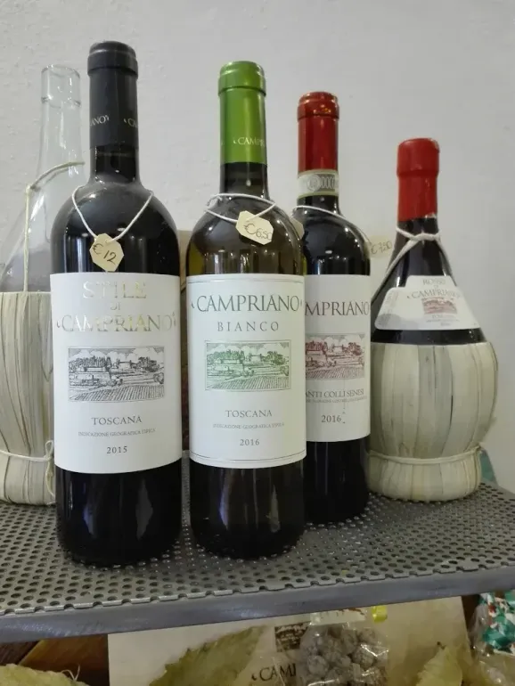 Quattro bottiglie di vino su uno scaffale, con tappi neri, verdi e rossi ed etichette bianche.