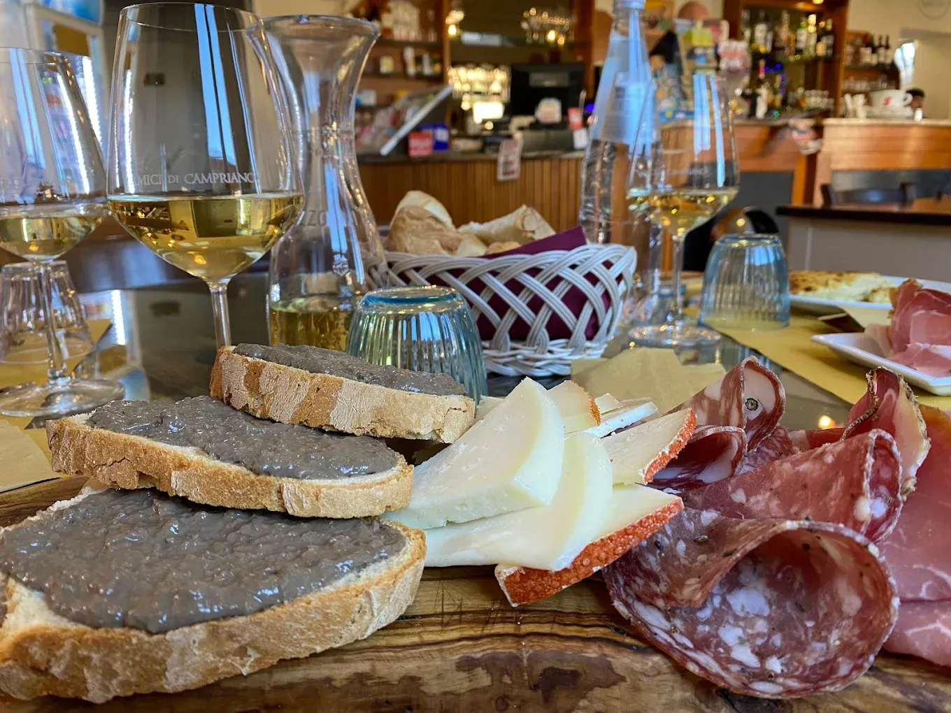 Tagliere di salumi e vino con pane, formaggio, salame affettato e un bicchiere in un'accogliente atmosfera da ristorante.
