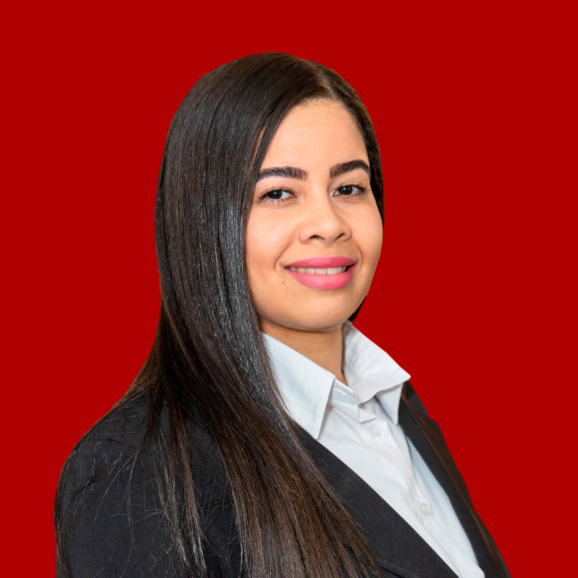 A woman in a suit and white shirt is standing in front of a red background.