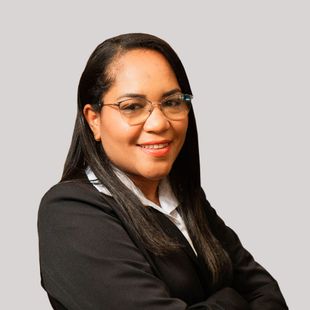 A woman wearing glasses and a black jacket is smiling with her arms crossed.