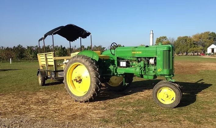 Green John Deere tractor pulling a wagon with a black canopy on a sunny day.