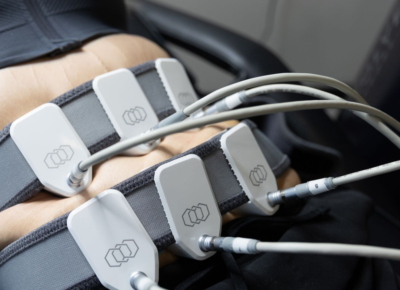 Person undergoing body contouring treatment with connected pads on abdomen.