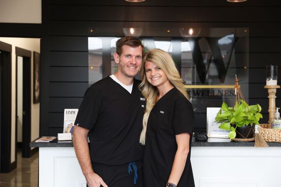 A man and a woman are posing for a picture in front of a reception desk.