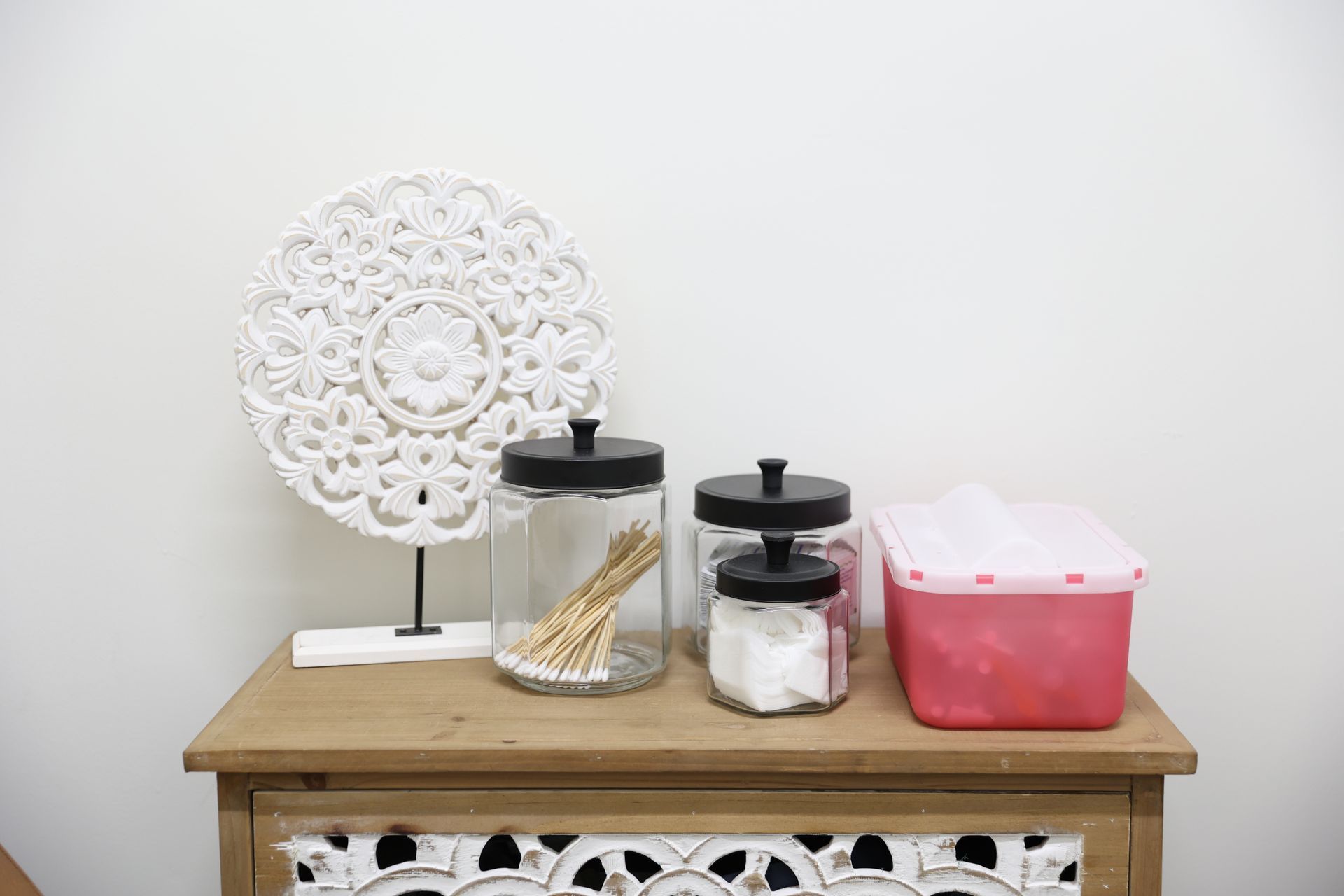 A wooden table with jars of cotton swabs , toothpicks , and a pink box on it.