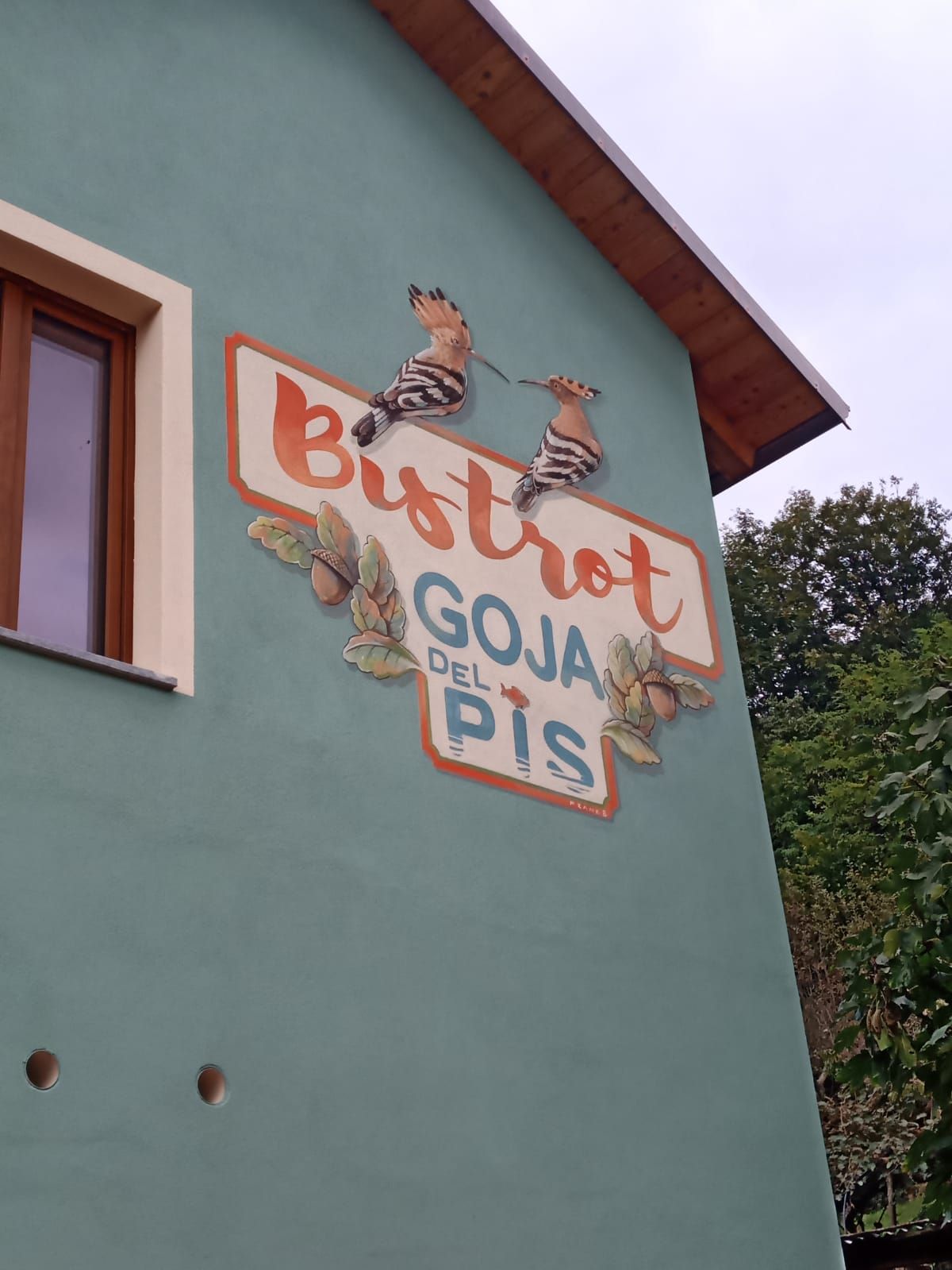 Insegna del Bistro Goya su una parete verde dell'edificio, decorata con uccelli dipinti e una grondaia rossa.