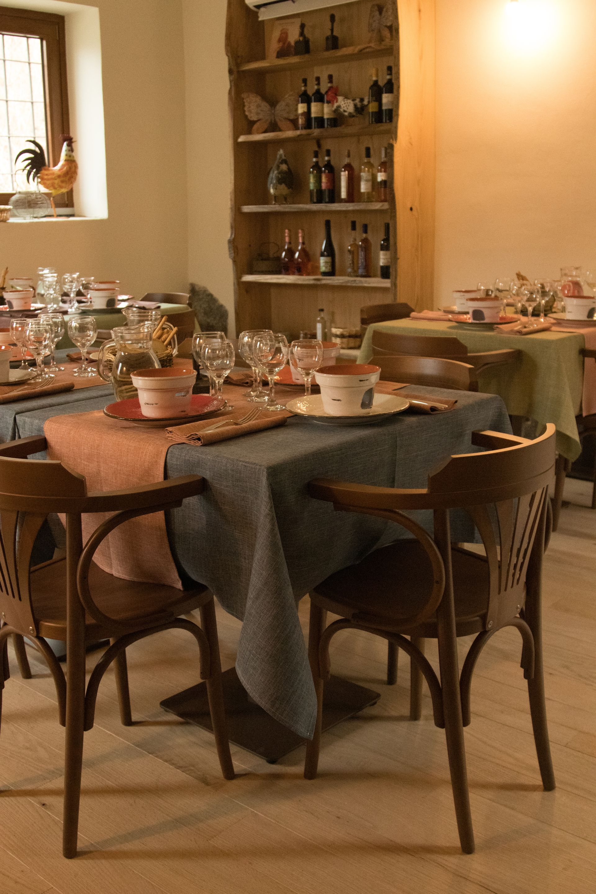 Tavoli apparecchiati con tovaglie grigie e color salmone per una cena in una stanza con una rastrelliera per il vino in legno.