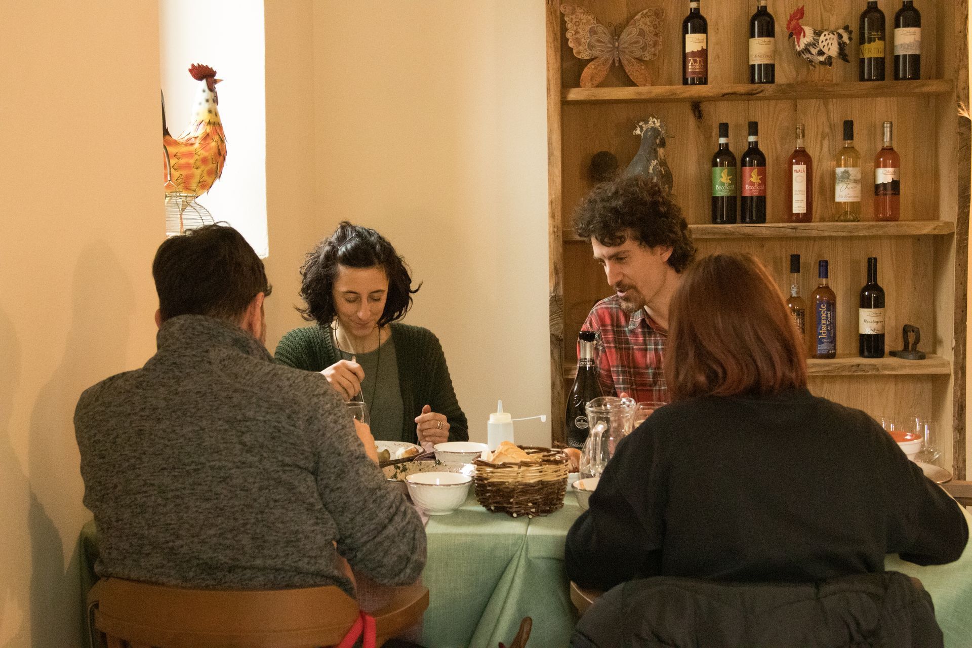Quattro persone sono sedute attorno a un tavolo di un ristorante, con bottiglie di vino esposte su scaffali di legno sullo sfondo.