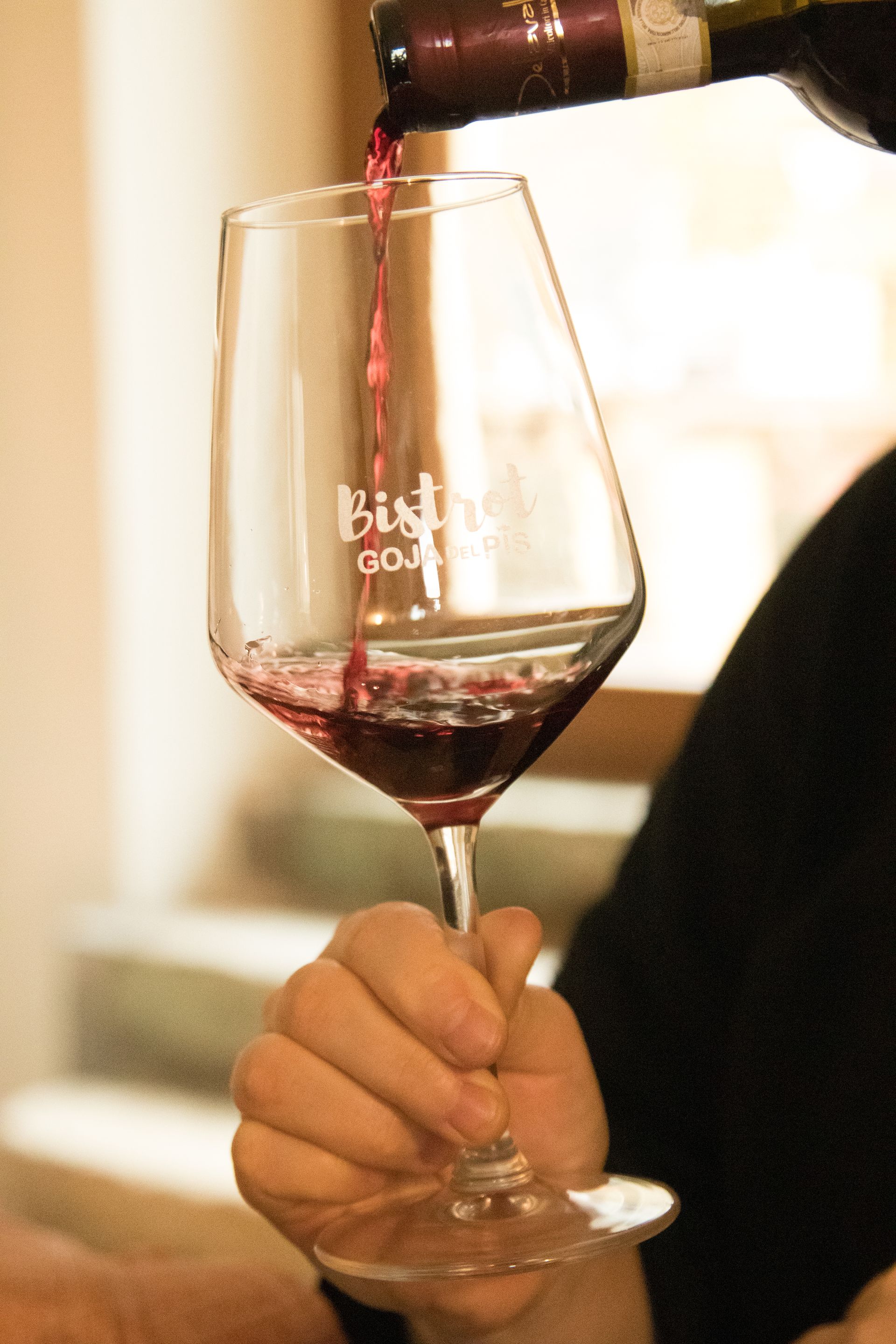 Una mano regge un calice di vino di marca mentre del vino rosso viene versato al suo interno da una bottiglia.