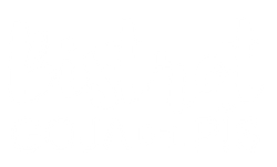 Primo piano di un piccolo cucciolo marrone e bianco seduto su un pavimento di legno, che guarda dritto in camera.