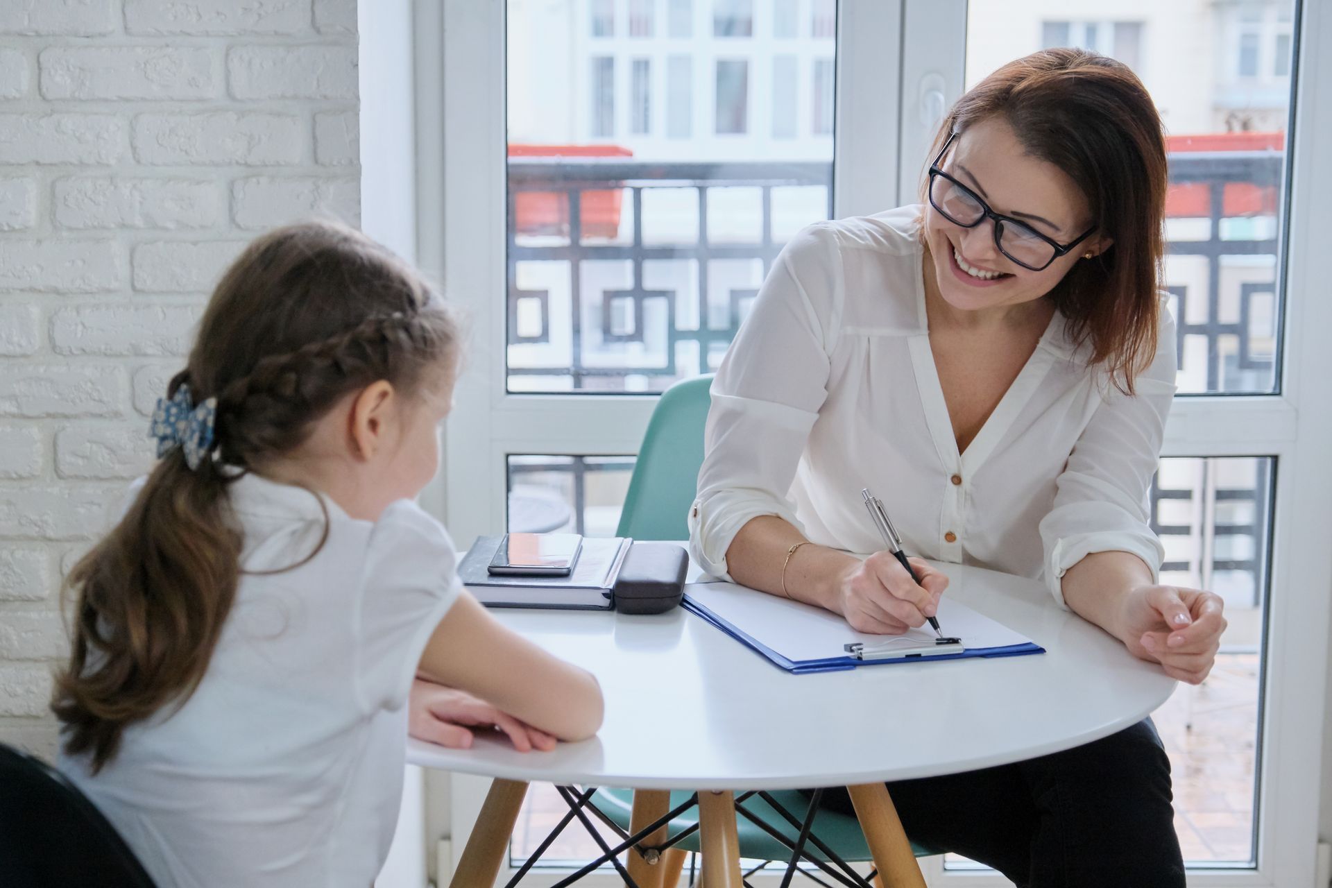 A woman is sitting at a table talking to a little girl.