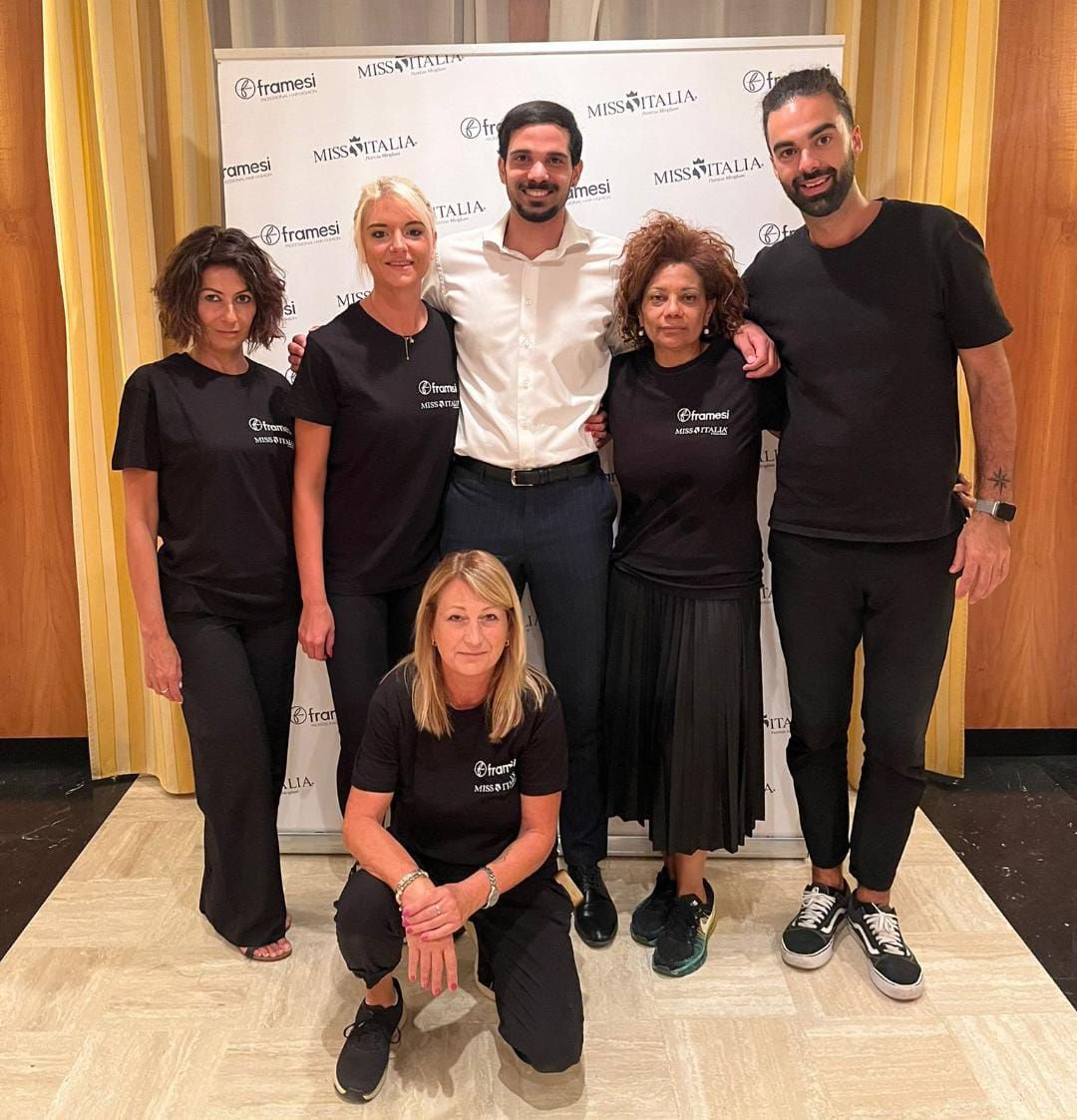 Un gruppo di persone in posa per una foto davanti a un muro su cui è scritto