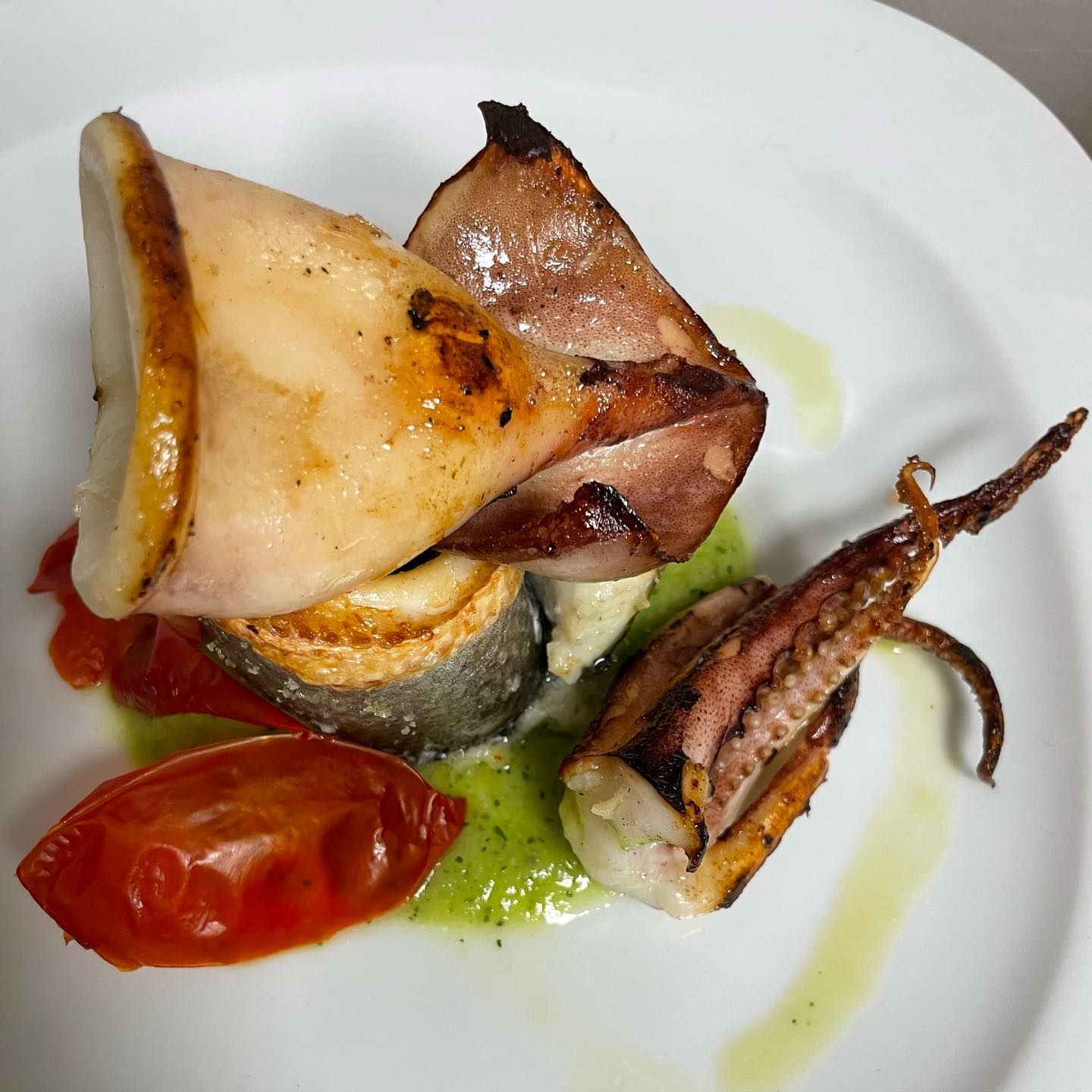 Calamari grigliati e pomodorini con salsa verde su un piatto bianco