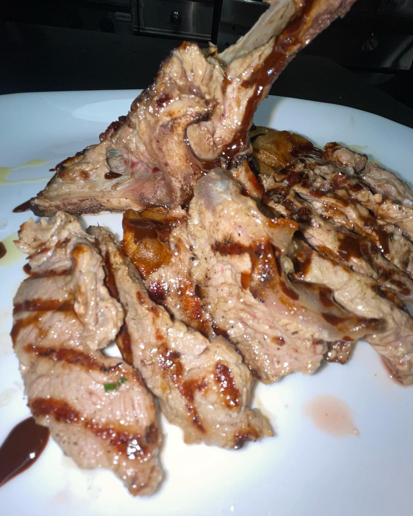 Carne grigliata a fette su un piatto bianco, sormontata da una costoletta con l'osso e salsa.