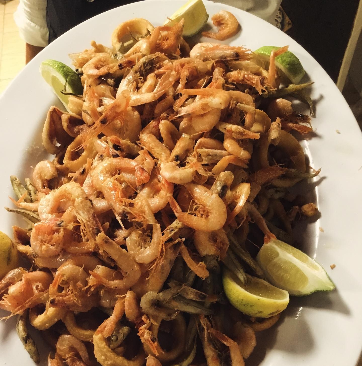 Piatto di gamberi o frutti di mare fritti, guarniti con cipolle e spicchi di lime, serviti su un piatto bianco.