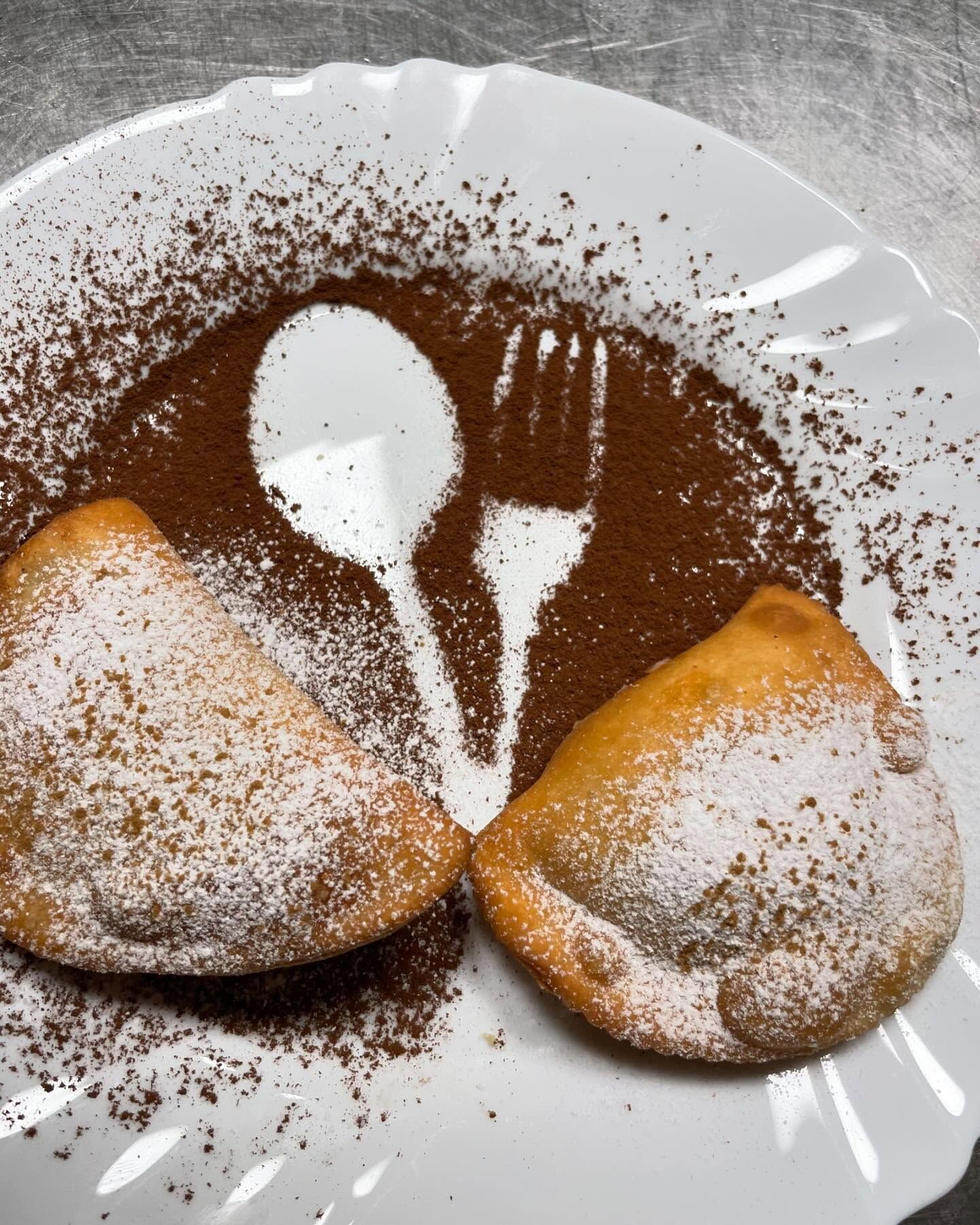 Due pasticcini ricoperti di zucchero a velo su un piatto bianco con una spolverata di cacao a forma di cucchiaio.