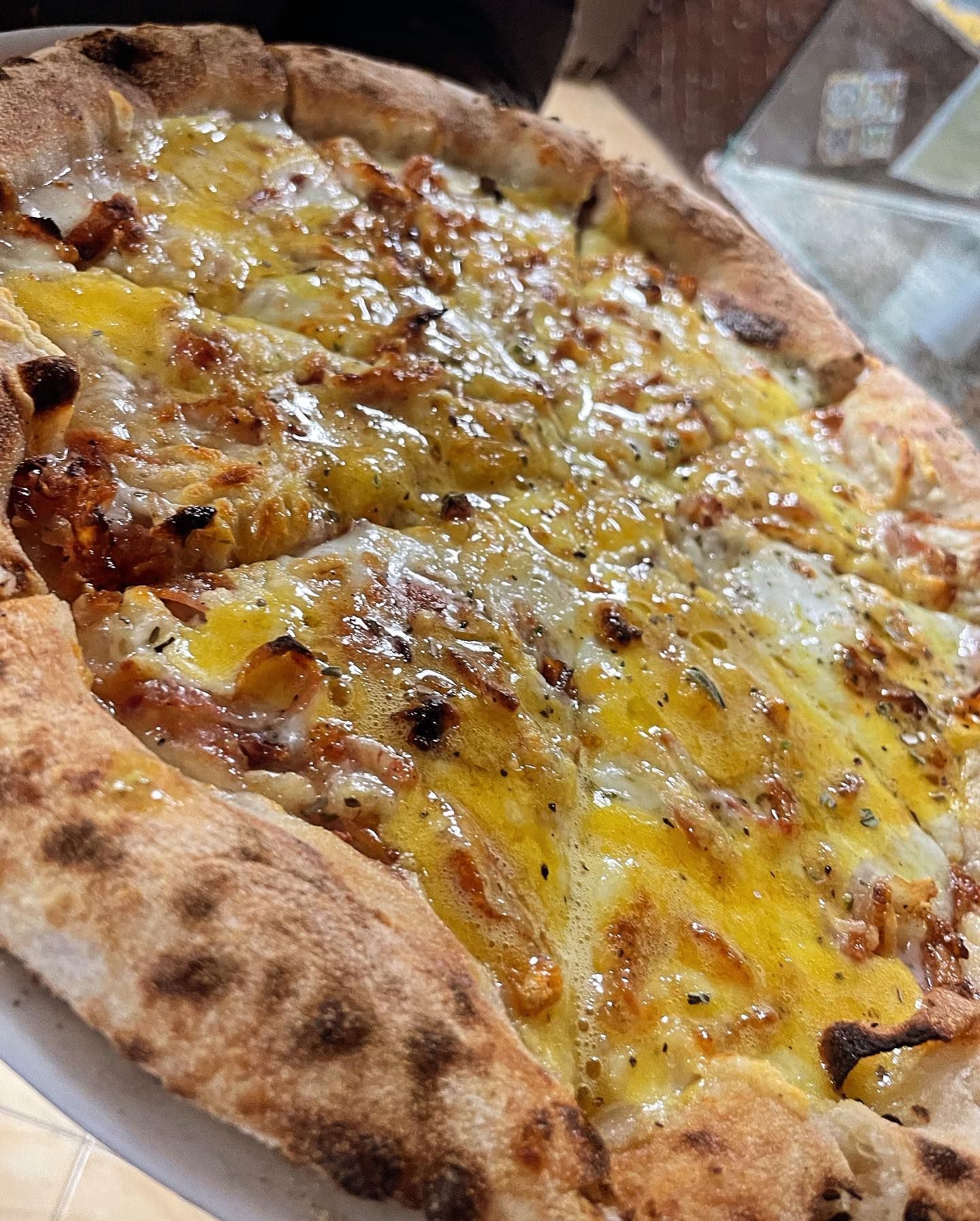 Primo piano di una pizza al formaggio con la crosta bruciacchiata su un piatto bianco.