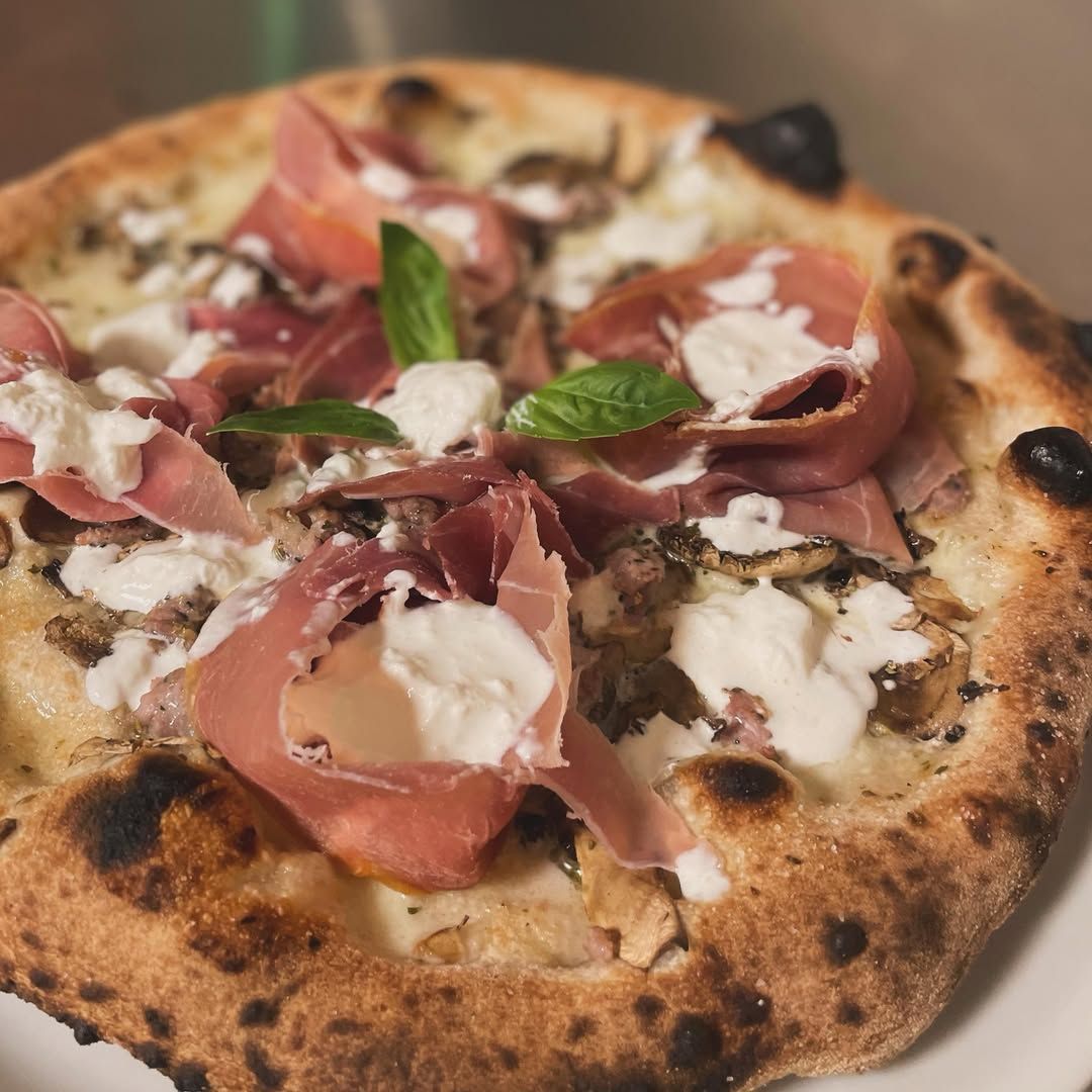 Pizza artigianale con prosciutto crudo, formaggio bianco, basilico e crosta bruciacchiata.