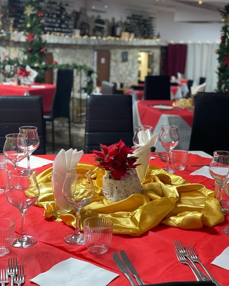 Tavolo da banchetto festivo con decorazioni rosse e dorate, bicchieri e centrotavola floreali in una sala da pranzo.
