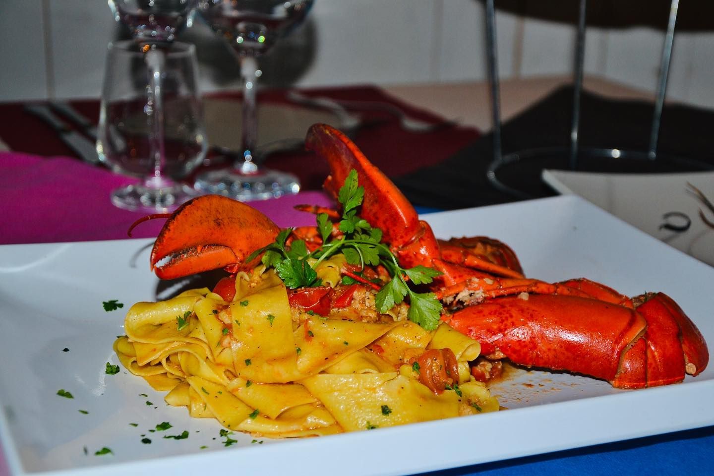 Pasta all'astice condita con erbe aromatiche su un piatto bianco in un ristorante dall'atmosfera soffusa.