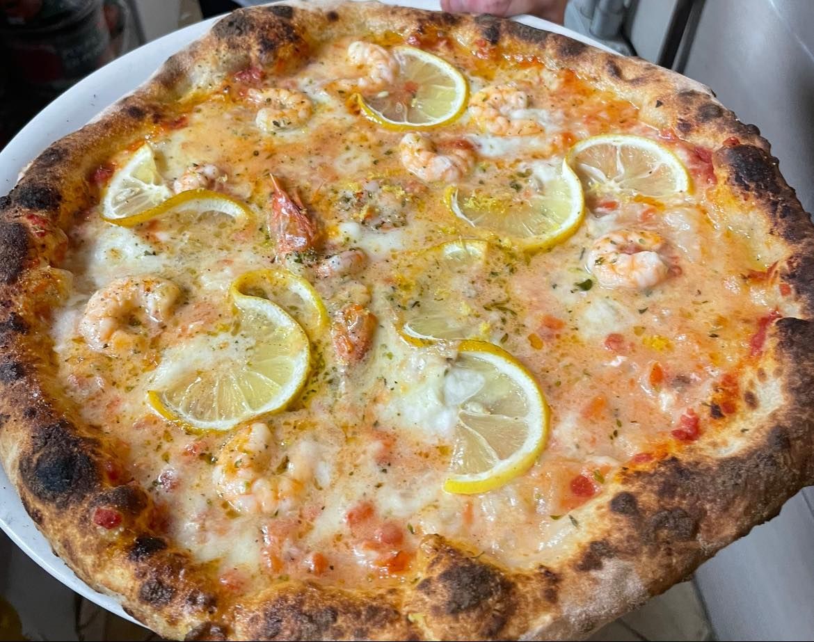 Pizza guarnita con fette di limone e formaggio fuso, cotta su una base rustica.