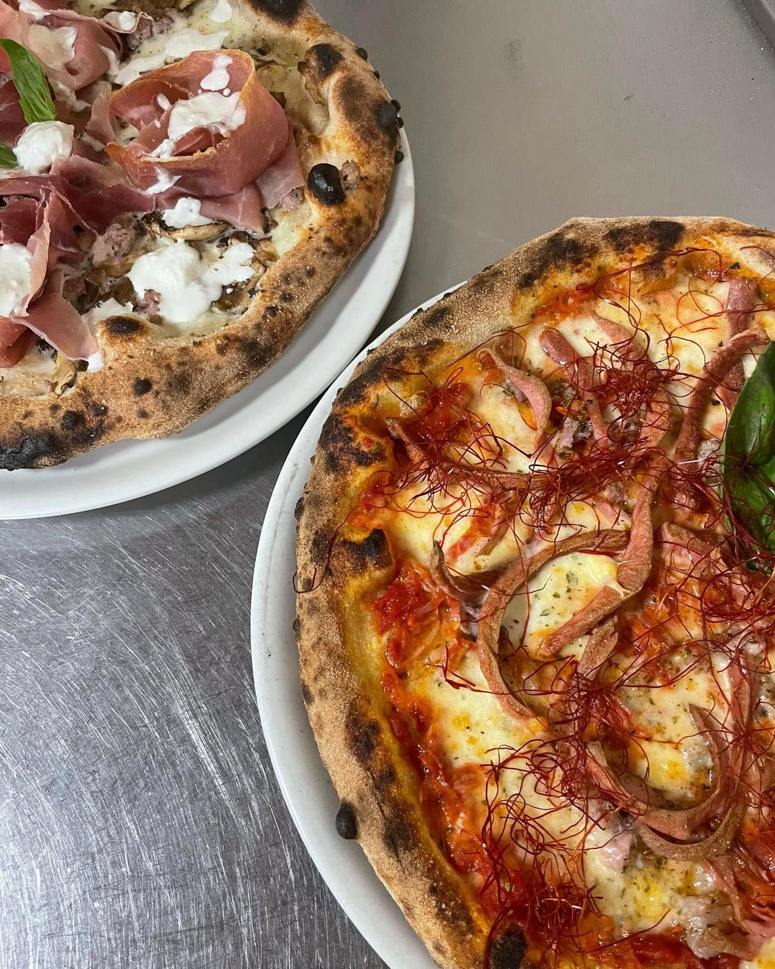 Due pizze su piatti bianchi, una con prosciutto e formaggio, l'altra con salsa di pomodoro e salame piccante.