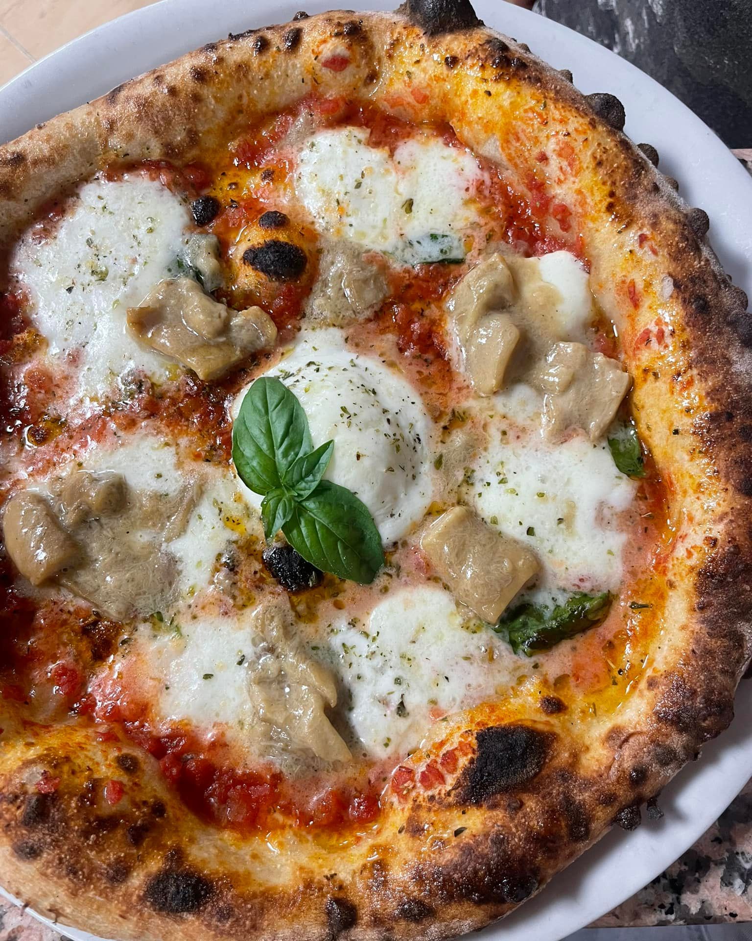 Pizza napoletana con mozzarella fusa, foglie di basilico e besciamella su un piatto