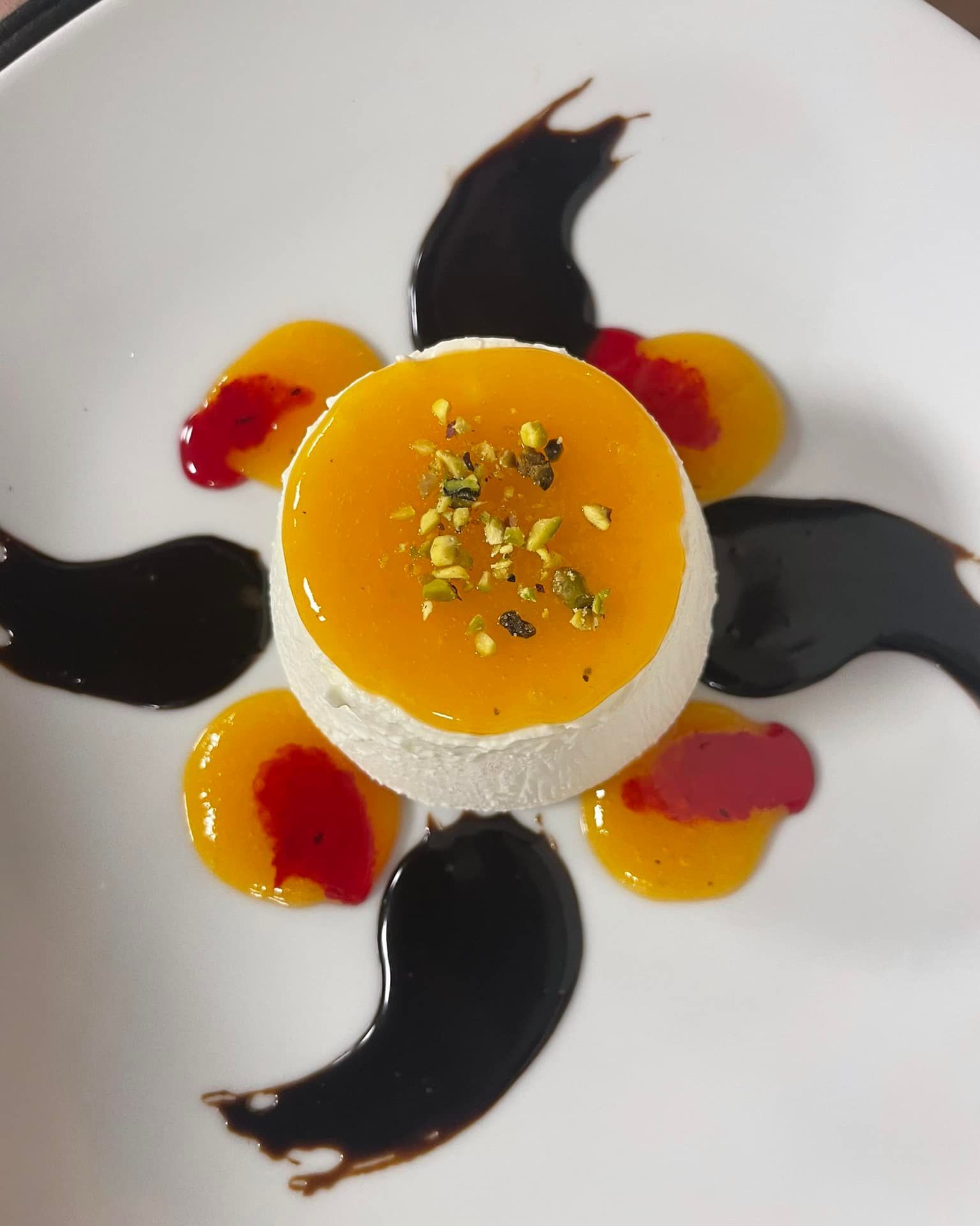 Dessert servito su un piatto bianco con gelatina di mango, salsa scura e guarnizioni.