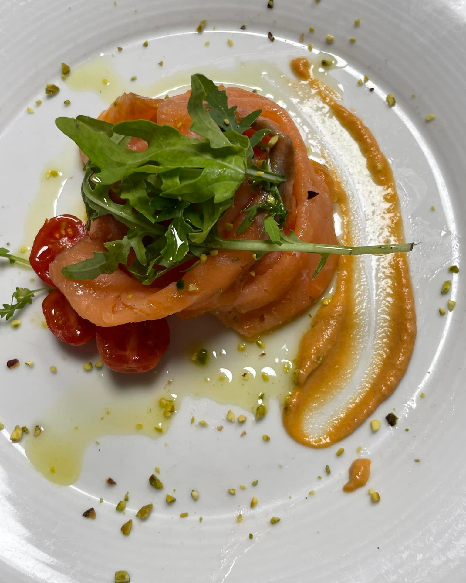 Salmone impiattato con verdure, pomodorini e salsa all'arancia su un piatto bianco.