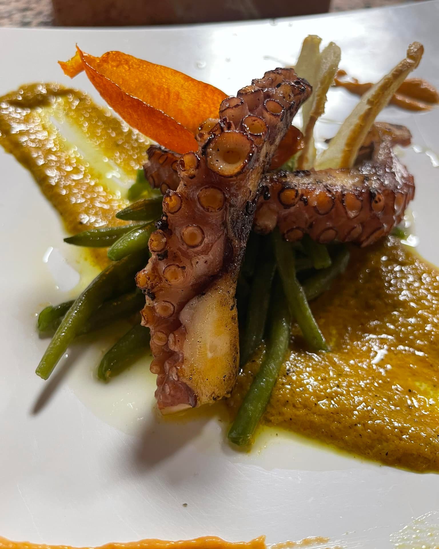 Polpo grigliato con fagiolini e salsa all'arancia su un piatto bianco.