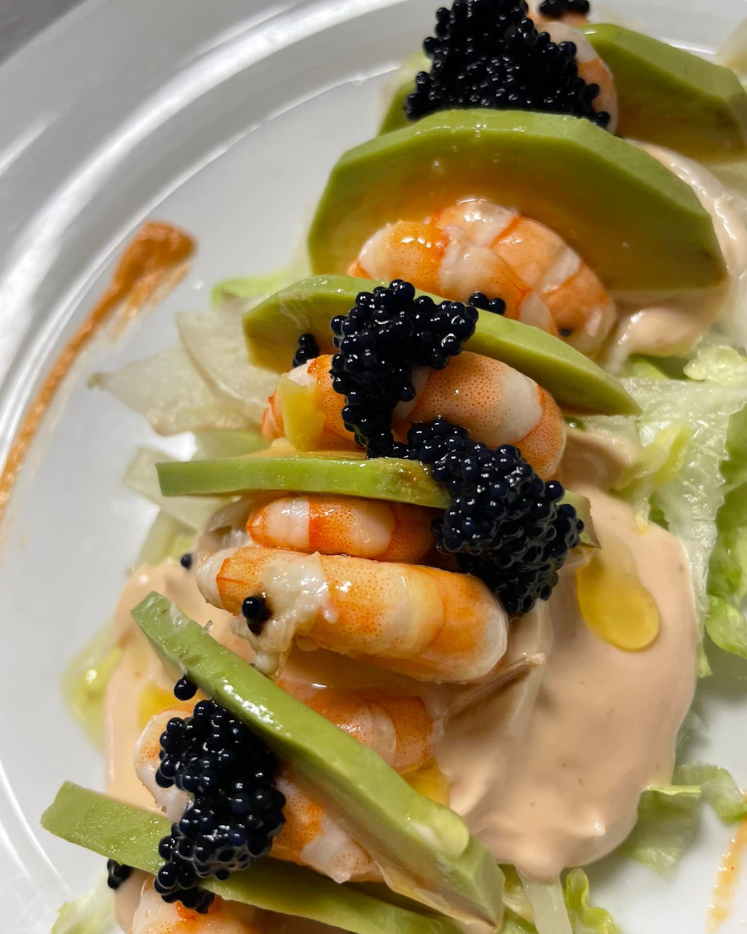 Antipasto di gamberi con fette di avocado e caviale nero su salsa cremosa
