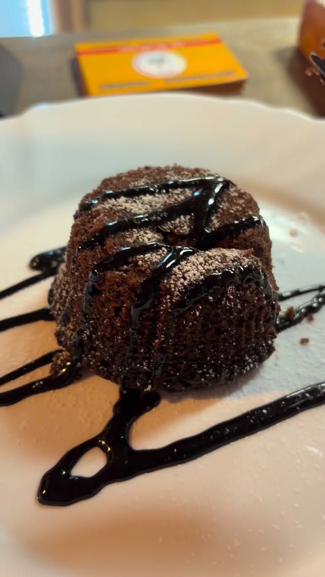 Torta al cioccolato fondente con cuore caldo, ricoperta di salsa al cioccolato, su un piatto bianco con sfondo sfocato.