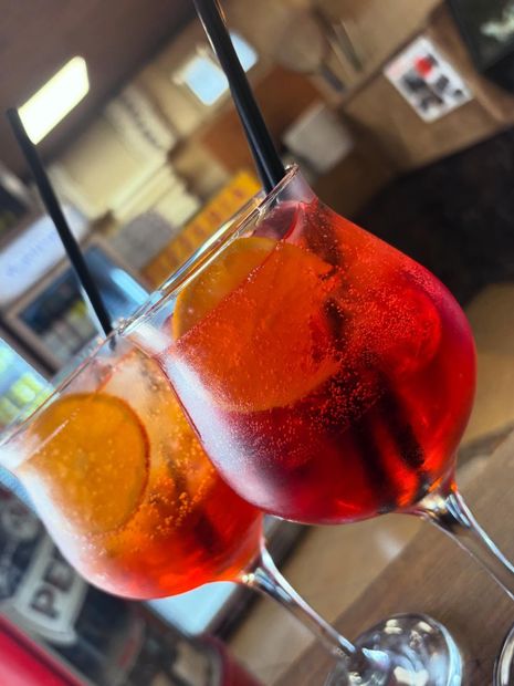 Due bicchieri con stelo contenenti cocktail rosso-arancio con cannucce nere, appoggiati su un tavolo da bar.