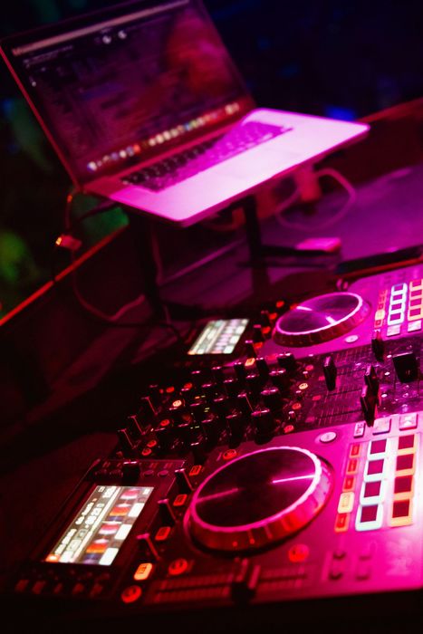 Computer portatile e controller da DJ sotto luci al neon rosa in un locale buio.
