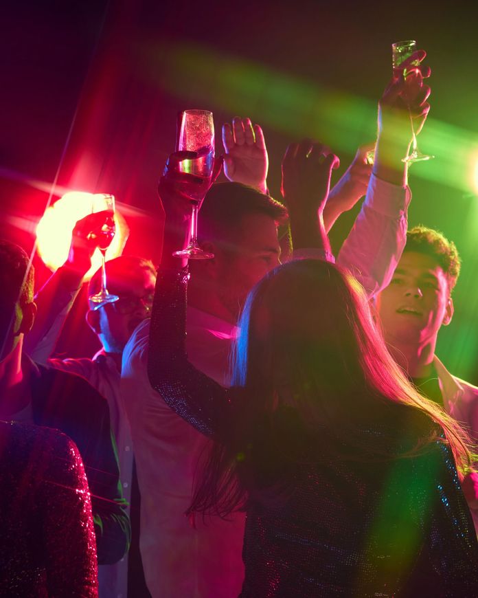 Persone che ballano con le mani alzate in un locale, illuminato da luci di scena rosse e verdi.