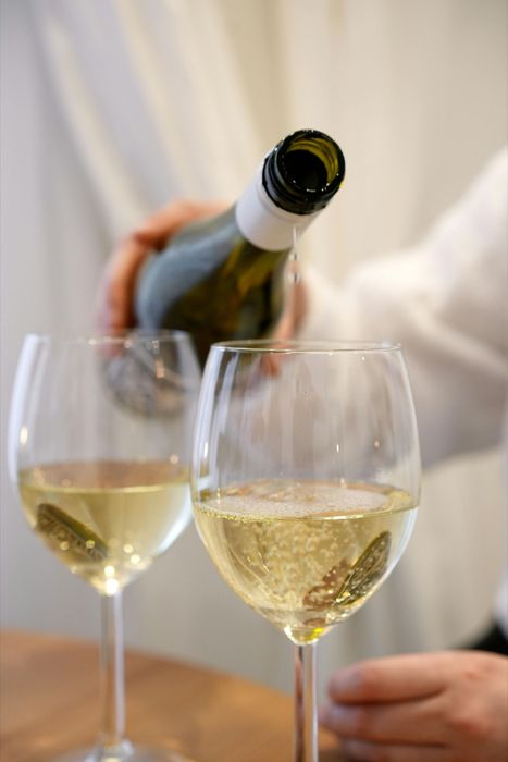 Una persona versa del vino bianco in due bicchieri a un tavolo.