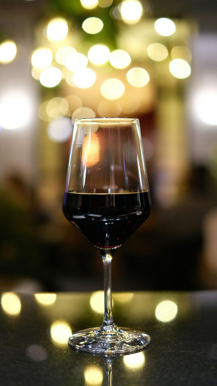 Un bicchiere di vino rosso su un tavolo con luci calde e sfocate sullo sfondo.