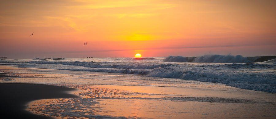 the sun is setting over the ocean and the waves are crashing on the beach .