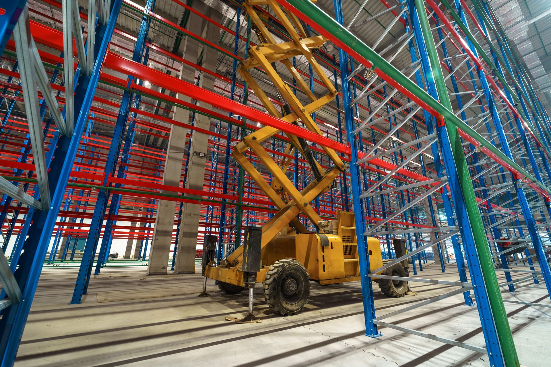 Un élévateur à ciseaux jaune se trouve dans un grand entrepôt.