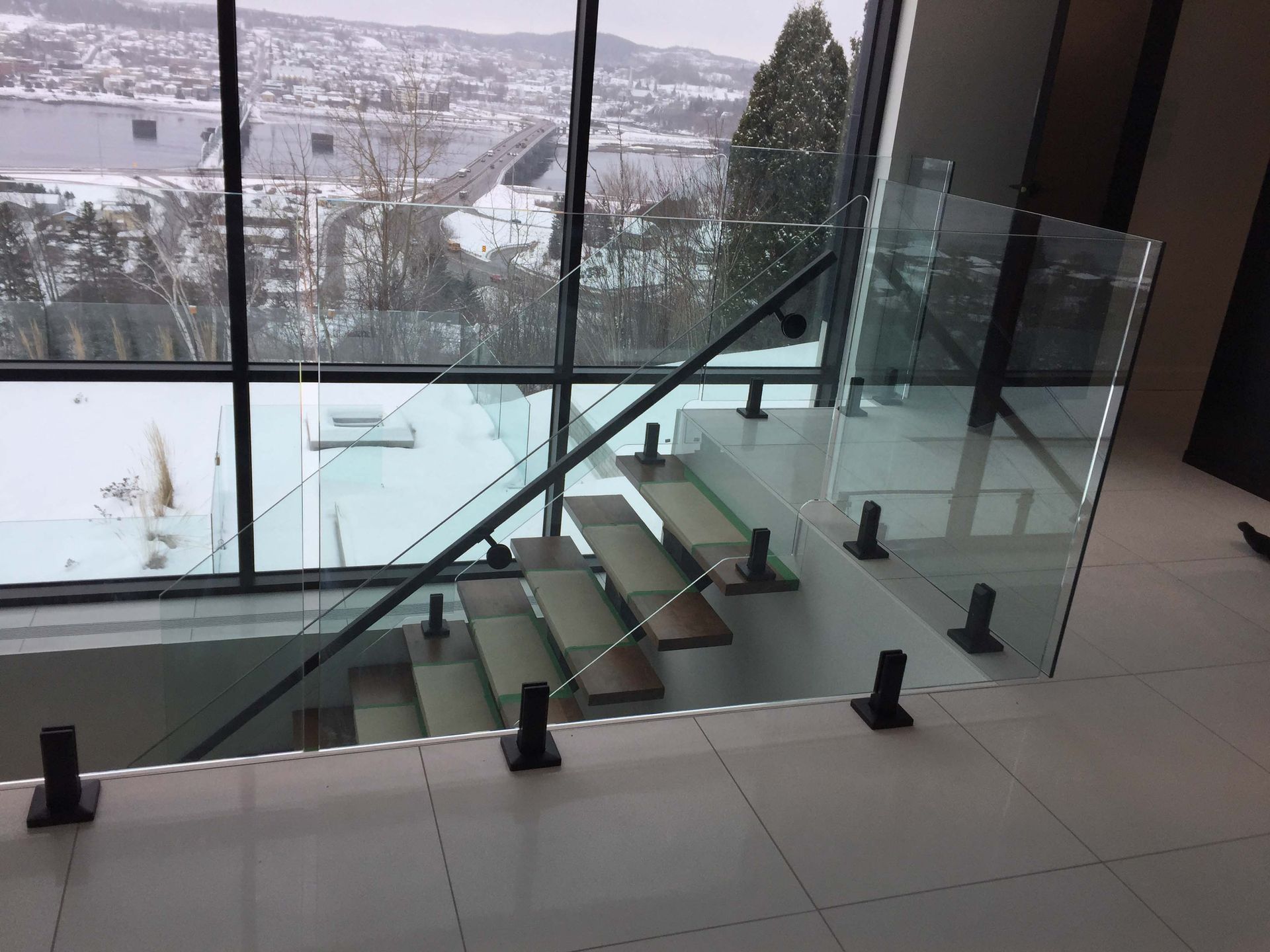 Un escalier avec une rampe en verre et une grande fenêtre.